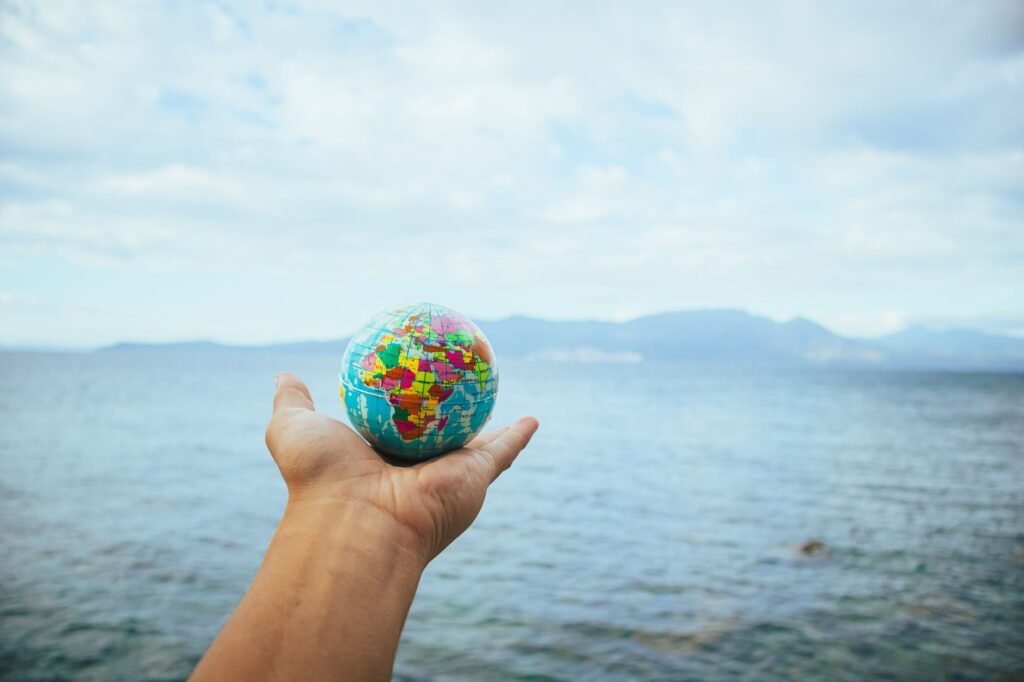 A hand holding a small globe in front of an ocean backdrop