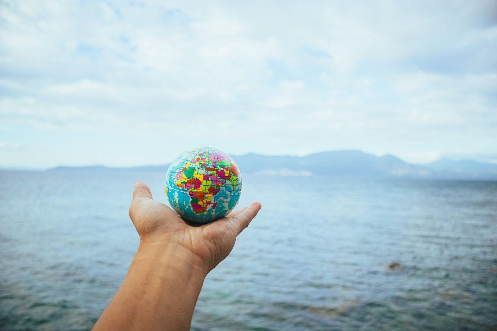 A hand holding a small globe in front of an ocean backdrop