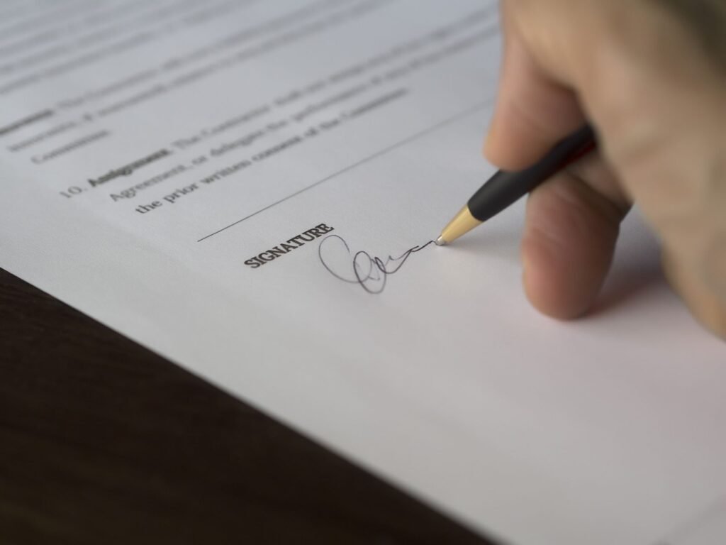 A hand signing a formal contract with a pen on a wooden desk