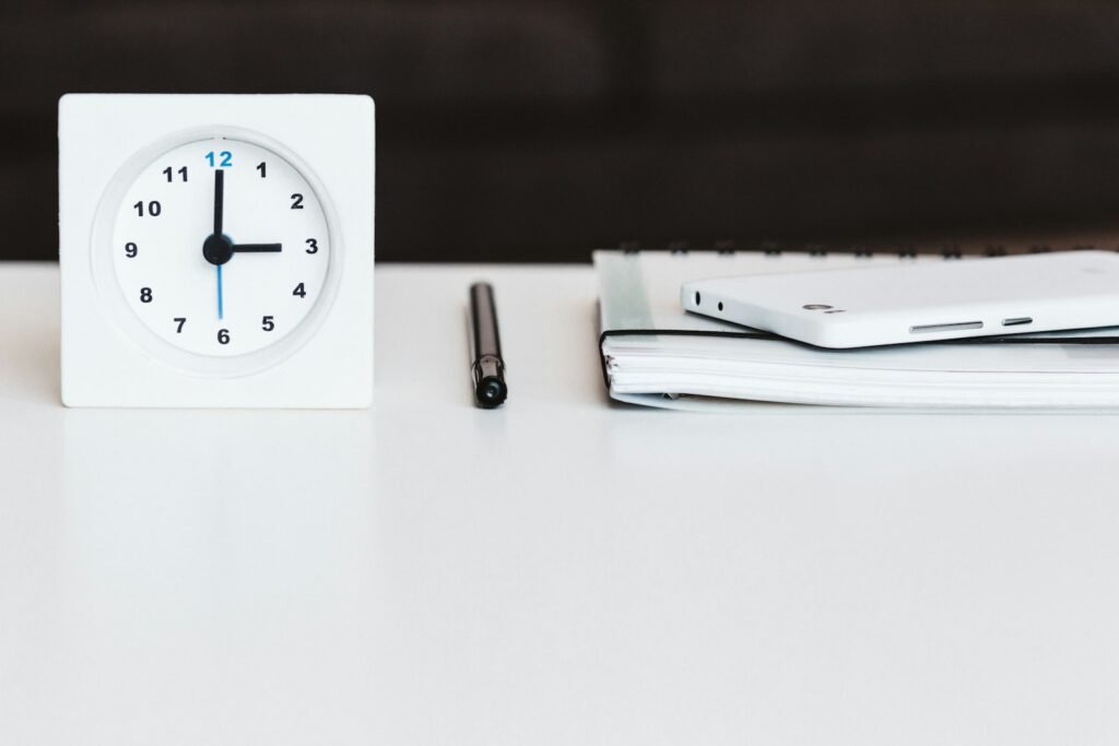 A white desk clock near a pen and a book